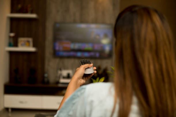 Woman using remote control changing channels or apps on smart TV
